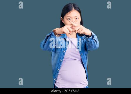 Junge schöne chinesische Frau schwanger schwanger schwanger schwanger schwanger Baby Ablehnung Ausdruck Überquerung Finger tun negative Zeichen Stockfoto