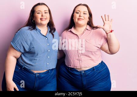 Junge Zwillinge in lässiger Kleidung zeigen und zeigen mit den Fingern Nummer fünf, während sie selbstbewusst und glücklich lächeln. Stockfoto