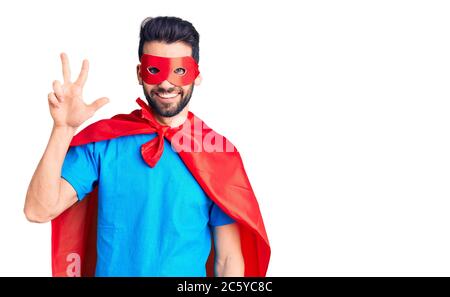 Junger schöner Mann mit Bart trägt Superhelden Kostüm zeigt und zeigt mit den Fingern Nummer drei, während lächelnd zuversichtlich und glücklich. Stockfoto