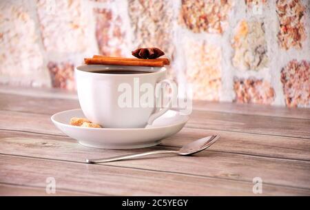 Eine Tasse schwarzen Kaffee auf einer Untertasse mit Zimt, Anis und Rohrzuckerscheiben. Nahaufnahme. Stockfoto