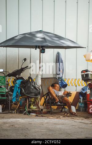 Saigon, Vietnam - 4. Juli 2020: In den Straßen von Saigon (Ho Chi Min City) schläft ein Mann, der ein Motorrad befestigt, auf dem Bürgersteig Stockfoto