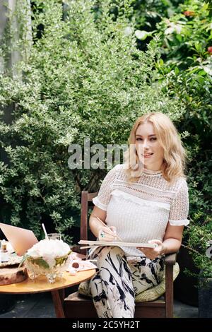Junger Geschäftsmann sitzt im Hinterhof ihres Hauses und Zeichnung Skizze von Kosmetikflaschen, die sie verkaufen wird Stockfoto