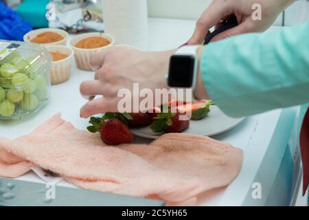 Mädchen Konditor schneidet frische Beeren mit einem Messer, um den Kuchen zu schmücken Stockfoto