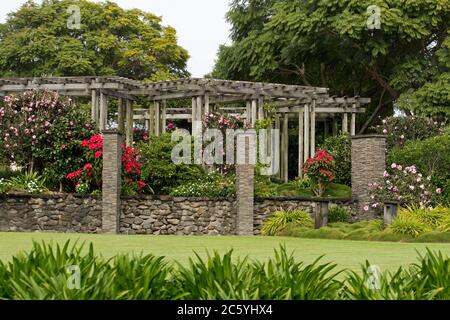 Farbenfroher Garten mit weitläufiger Pergola mit Steinmauer und Säulen mit blühenden Sträuchern und Kamelien, umgeben von Rasen und schattenspendenen Bäumen in Australien Stockfoto