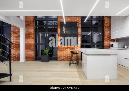 Loft-Stil Wohnung mit weißer Küche mit Insel, große Fenster, Backsteinwände und LED-Deckenleuchte Stockfoto