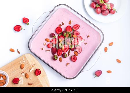 Draufsicht auf köstlichen cremigen Beerensouffle Kuchen in einer Glasschale mit Erdbeeren und Mandeln auf weißem Tisch. Leckeres, gesundes Frühstück Stockfoto