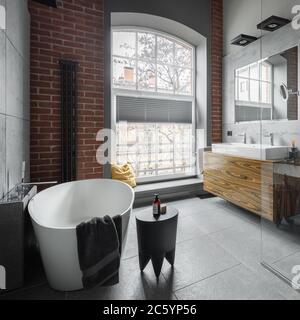 Badezimmer im Industriestil mit ovaler Badewanne und großem Fenster Stockfoto