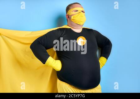 Reinigung Superheld rettet die Welt vor Schmutz, Mann hat Ente Bild auf Kostüm, er ist in gelber Kleidung und in Schutzhandschuhe, posiert isoliert über blu Stockfoto