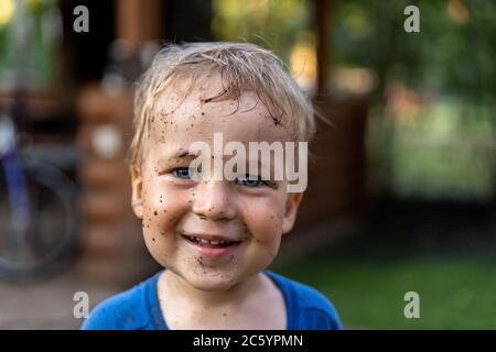 Niedliche liebenswert blonde kaukasischen kleinen glücklich Kleinkind Junge Porträt mit chaotisch Mus Flecken auf Gesicht nach dem Spielen Bewässerung Garten auf Hof oder Grafschaft Bauernhof Stockfoto