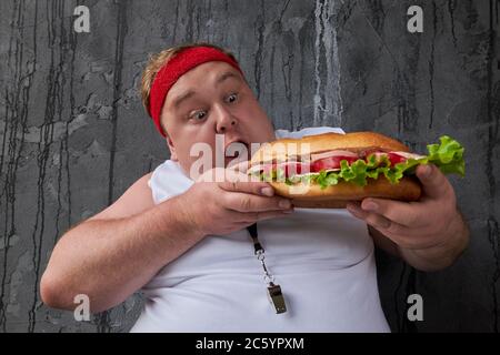 Fat lustige Mann öffnete seinen Mund, um ein Leckerbissen von einem Sandwich beißen. Hungrige männliche führt ungesunde Lebensweise, Ernährungskonzept Stockfoto