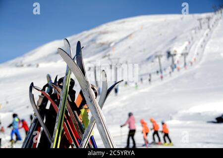 Skiausrüstung auf verschwommenem Hintergrund von Skifahrern, Schnee, Pisten, Skilift in der alpinen Sonne des Piemont. Stockfoto