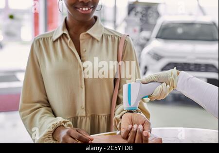 Autohaus Mitarbeiter, Arzt prüft die Temperatur des Kunden in Autos Showroom, er verwenden spezielle Vorrichtung, legt es in die Hand Stockfoto