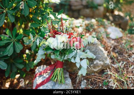 brautstrauß aus Burgunder Pfingstrosen, roten Rosen, Eukalyptusbäumen, Eryngium, Babyluft, Celosia und roten Bändern auf dem Stein Stockfoto