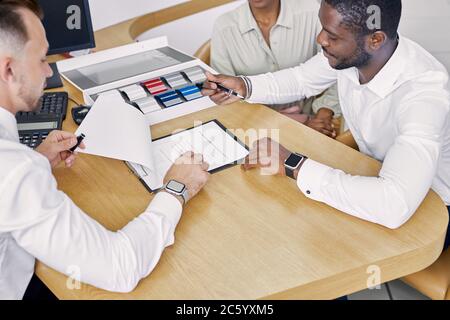 Schwarze Kunden unterzeichnen einen Vertrag, während sie am Tisch mit Verkäufer sitzen, erklären professioneller Arbeiter des Händlerbetriebs Bedingungen des Vertrages und zeigen, wo man Stockfoto