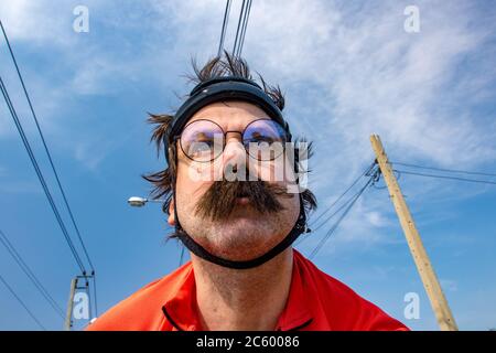 Porträt von Radfahrer im Retro-Helm Fahrrad fahren in der Sommerlandschaft, blauer Himmel Hintergrund. Der Erwachsene Biker mit Schnurrbart fahren auf Rennrad unter c Stockfoto