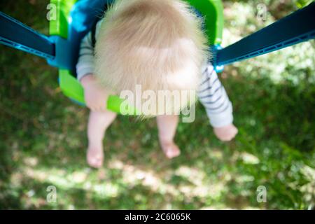 Ein kleiner Junge, der Spaß hat, auf einer Schaukel unter einem Baum in einem Garten zu spielen Stockfoto