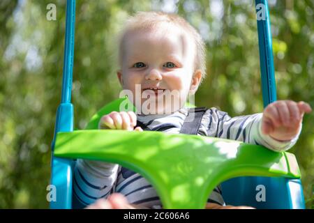 Ein kleiner Junge, der Spaß hat, auf einer Schaukel unter einem Baum in einem Garten zu spielen Stockfoto