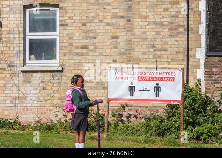 London, UK - 16 June, 2020 - Social Distanzing Zeichen mit einer Anzeige von 2 Meter Entfernung in einem Park mit einem Mädchen, das einen Roller durch Stockfoto