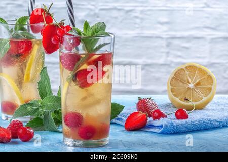 Ein erfrischendes Sommergetränk mit Erdbeeren, Kirschen, Johannisbeeren und Zitrone in Gläsern auf einem Tisch Stockfoto