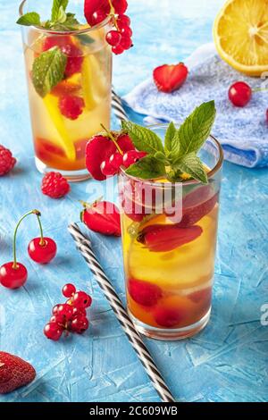 Ein erfrischendes Sommergetränk mit Erdbeeren, Kirschen, Johannisbeeren und Zitrone in Gläsern auf einem Tisch Stockfoto