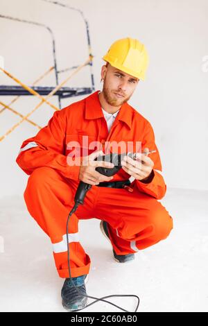 Junger Vorarbeiter in orange Arbeitskleidung und gelben Hardhat thoughtf Stockfoto