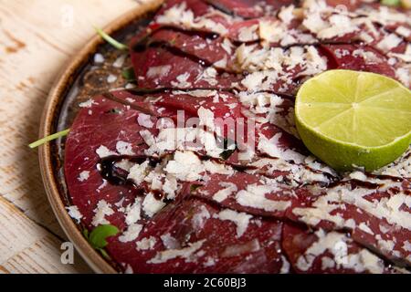 Nahaufnahme von Rindfleisch Carpaccio mit Parmesan und Rucola mit einer halben Limette verziert. Stockfoto