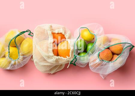 Früchte und Zitronen in wiederverwendbaren, umweltfreundlichen Netzbeuteln auf rosa Hintergrund. Kein Verschwendung einkaufen. Stockfoto