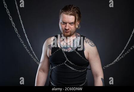 Foto eines tätowierten jungen Mannes, der in Ketten gebunden ist Stockfoto