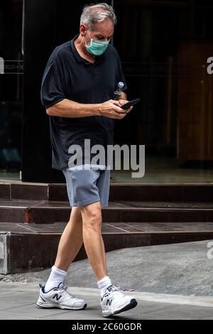 Mann mit Gesichtsmaske und Mobiltelefon auf der Straße während der Pandemie 19 in Bangkok, Thailand Stockfoto