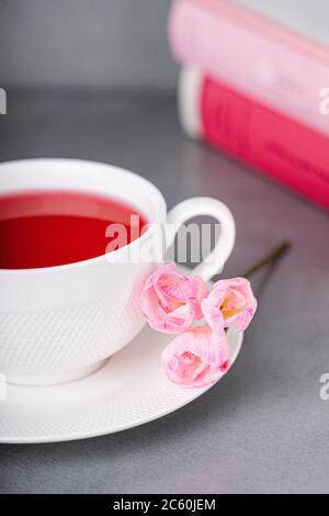 Himbeer-Tee, rosa Freesia-Blumen und Bücher auf grauem Hintergrund Stockfoto
