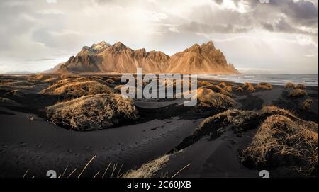 Vestrahorn Berge und Stokksnes Strand in der Nähe von Hofn, Süd-Island. Gräser und schwarzer Gesang bei Ebbe während der goldenen Stunde. Stockfoto