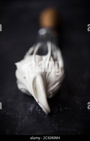 Handballon Schneebesen mit geschlagenem Ei weißen Meringue Mischung. Nahaufnahme auf schwarzem Hintergrund. Stockfoto