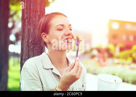 Glückliche junge Frau essen frischen Salat im Stadtpark, im Freien Stockfoto