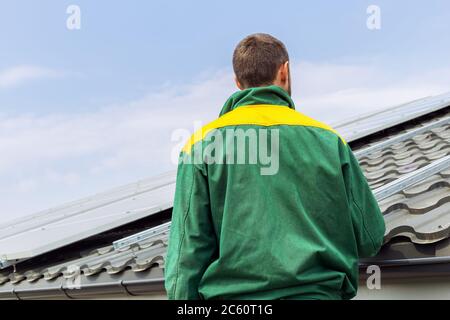 Mann Arbeiter Ingenieur gegen Solarzellen-Station auf Hausdach. Rückansicht unkenntlich Silhouette. Alternative Energie ökologisches Konzept. Stockfoto