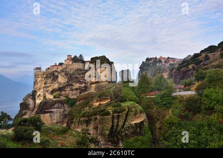 Meteora Klöster. Schöne Aussicht auf das Heilige Kloster von Varlaam auf dem Rand des hohen Felsen von den Morgenwolken und Nebel bei Sonnenaufgang bedeckt platziert Stockfoto