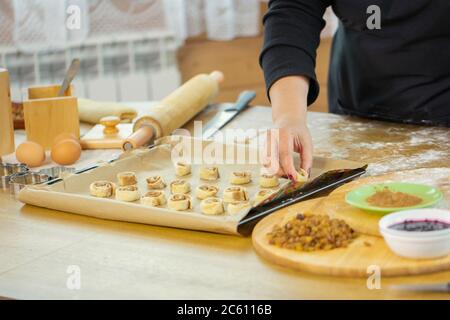 Close-up weibliche Hand legt Zimtbrötchen auf Backblech mit Pergamentpapier Stockfoto