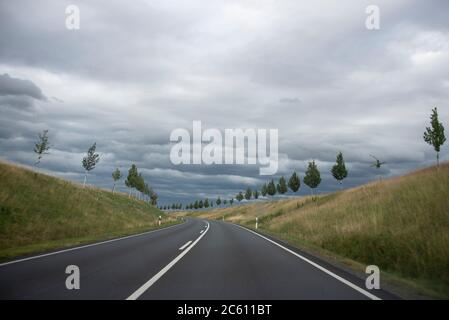 05. Juli 2020, Sachsen-Anhalt, Gernrode: Dunkle Wolken hängen über einer Landstraße bei Gernrode im Harz. Links und rechts der Straße biegen sich kleine Bäume im Wind. Foto: Stephan Schulz/dpa-Zentralbild/ZB Stockfoto