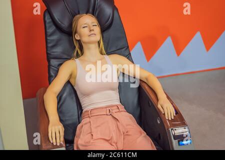 Schöne junge Frau, die sich auf dem Massagesessel am Flughafen oder im Einkaufszentrum entspannt Stockfoto