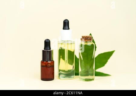 Glasflaschen mit pflanzlichem CBD-Öl, THC-Tinktur und Hanfblatt auf pastellbeigem Hintergrund. Flaches Design, minimaler Stil. Kosmetik CBD-Öl. Ätherische Naturöle für Gesicht und Körper. Stockfoto