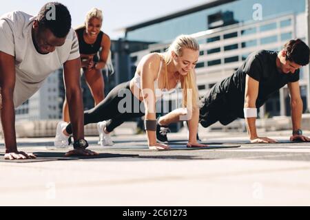 Fitness-Männer und -Frauen, die Liegestütze mit Motivation von ihrer Trainerin im Freien in der Stadt machen. Stockfoto