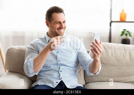 Glücklicher Mann, der zu Hause Smartphone benutzt Stockfoto