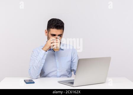 Beschäftigt elegante junge Mann Mitarbeiter sitzen im Büro Arbeitsplatz, arbeiten auf Laptop, um alle seine Arbeit zu erledigen früh am Morgen mit einer Tasse Kaffee. indoo Stockfoto