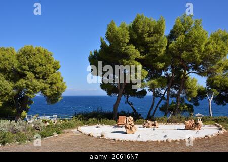 Garten mit Picknicktisch und Stühlen und Ruhebereich unter Pinien an der Küste der Ägäis bei Sonnenuntergang, Attika, Griechenland Stockfoto