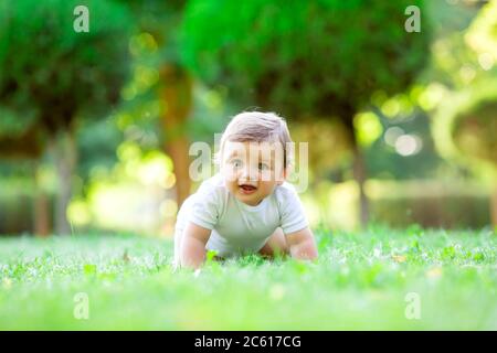 Niedliches Kind in weißem Body lernt zu kriechen. Gesundes Kleinkind kriecht im Sommer auf grünem Gras Stockfoto