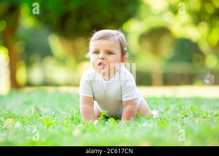 Niedliches Kind in weißem Body lernt zu kriechen. Gesundes Kleinkind kriecht im Sommer auf grünem Gras Stockfoto