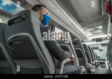 Kaukasische Männer in Sicherheitsmaske Sitzgelegenheit im Shuttlebus während der Pandemie. Thema Öffentliche Verkehrsmittel. Stockfoto