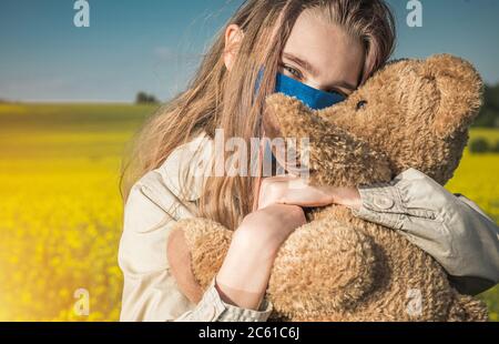 Portrait von Happy Caucasian Teenage Girl in Face Maske Umarmung ihrer Teddybär während Pandemie. Thema „Virenausbruch“. Stockfoto