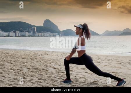 Südamerika, Brasilien, Copacabana Beach. Eine schwarze Brasilianerin in den frühen Dreißigern, die sich vor einem Lauf dehnt Stockfoto