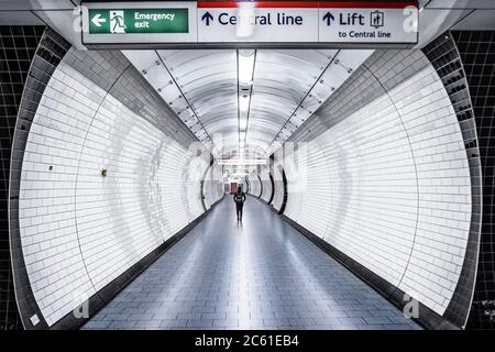 Eine Frau, die einen leeren Durchgang in einer Station der Central Line der Londoner U-Bahn-Linie entlang läuft Stockfoto