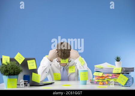 Überarbeiteter Geschäftsmann greifen auf seinen Kopf mit Terminnotizen rund um Büro Stockfoto